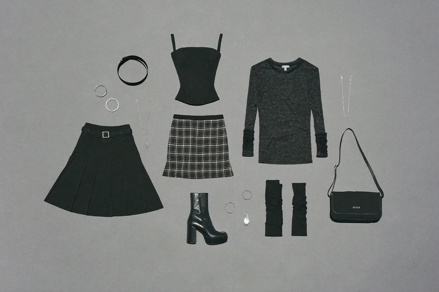 Flat lay of alt wardrobe essentials: pleated skirt, plaid skirt, corset top, mesh top, tights, platform boots and silver jewellery