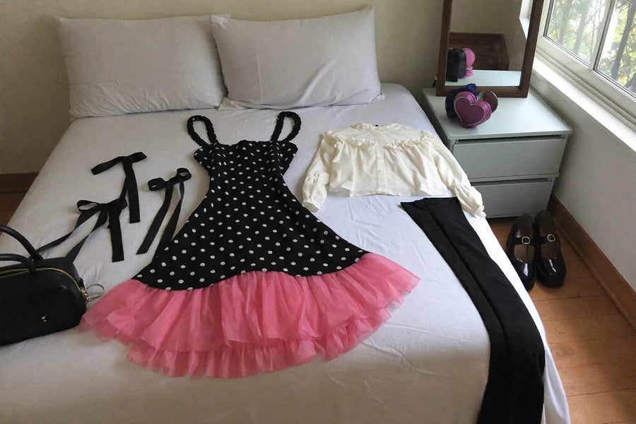 Jirai Kei outfit laid out on a bed: black and pink pinafore dress, ruffled blouse, tights and Mary Jane platforms