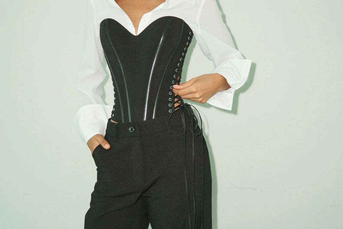 Structured black corset top styled over a white shirt with high-waisted trousers