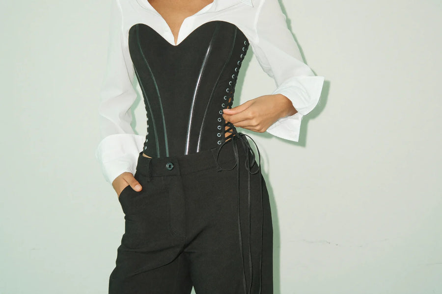 Structured black corset top styled over a white shirt with high-waisted trousers