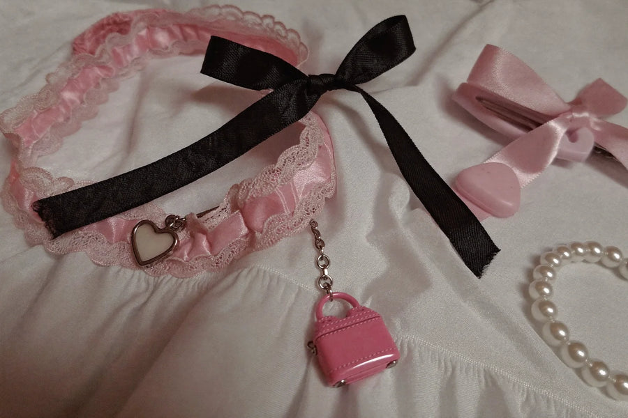 Jirai Kei accessories flat lay with pink and black satin ribbons, a heart pendant lace choker and hair clips