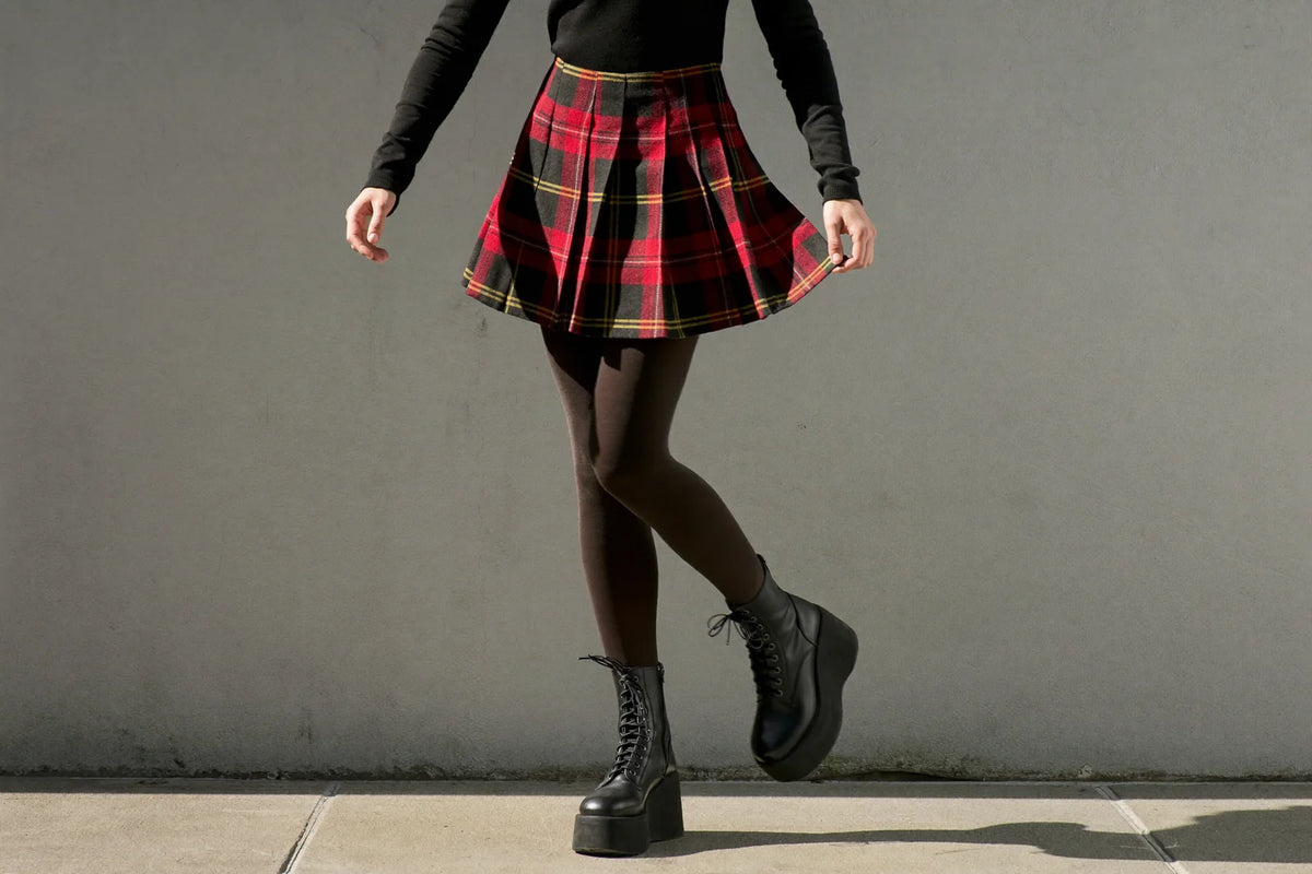 Red and black plaid pleated mini skirt styled with a black top, tights and platform boots