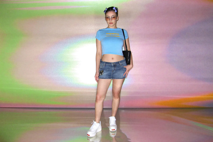 Y2K outfit with a cropped baby tee, low-rise denim mini skirt and chunky white platform trainers